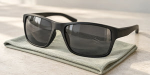 Illustration of fine scratches on a dark sunglass lens, with the frame resting on a microfiber cloth.